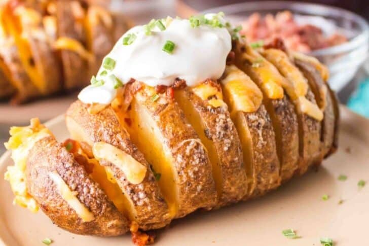 Sliced baked potato with melted cheese, topped with sour cream and chopped chives, served on a plate.