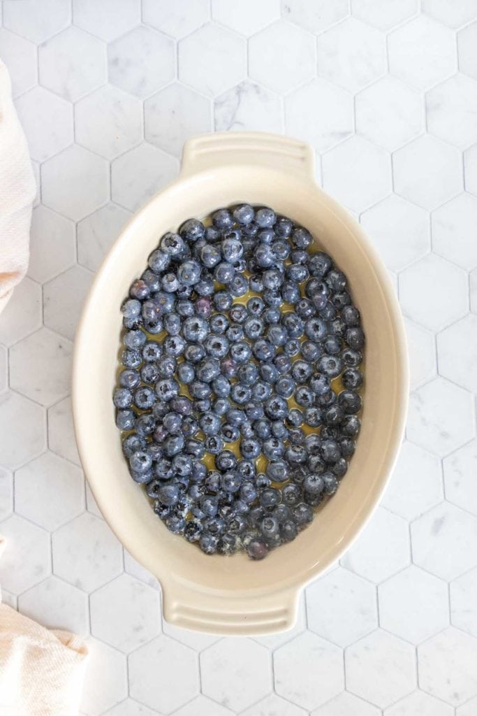 Oval ceramic dish filled with fresh blueberries, set on a white hexagon tile surface.