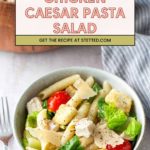 A bowl of chicken Caesar pasta salad with penne, lettuce, cherry tomatoes, croutons, parmesan, and black pepper. A recipe title and website appear above the bowl.