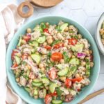 A bowl of salad containing chickpeas, cherry tomatoes, cucumber, red onion, tuna, and mixed greens on a white hexagon-tiled surface.