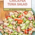 A bowl of chickpea tuna salad with chopped cucumber, cherry tomatoes, red onion, and herbs, shown with a wooden spoon.