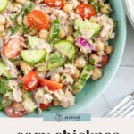 A bowl of chickpea tuna salad with cherry tomatoes, cucumbers, and herbs sits on a marble surface next to a fork. Text below reads, "easy chickpea tuna salad.