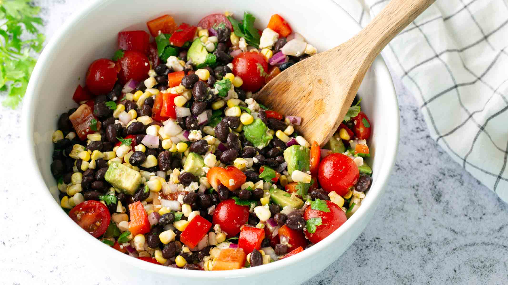 A serving bowl of corn and black bean salad with a spoon in it.