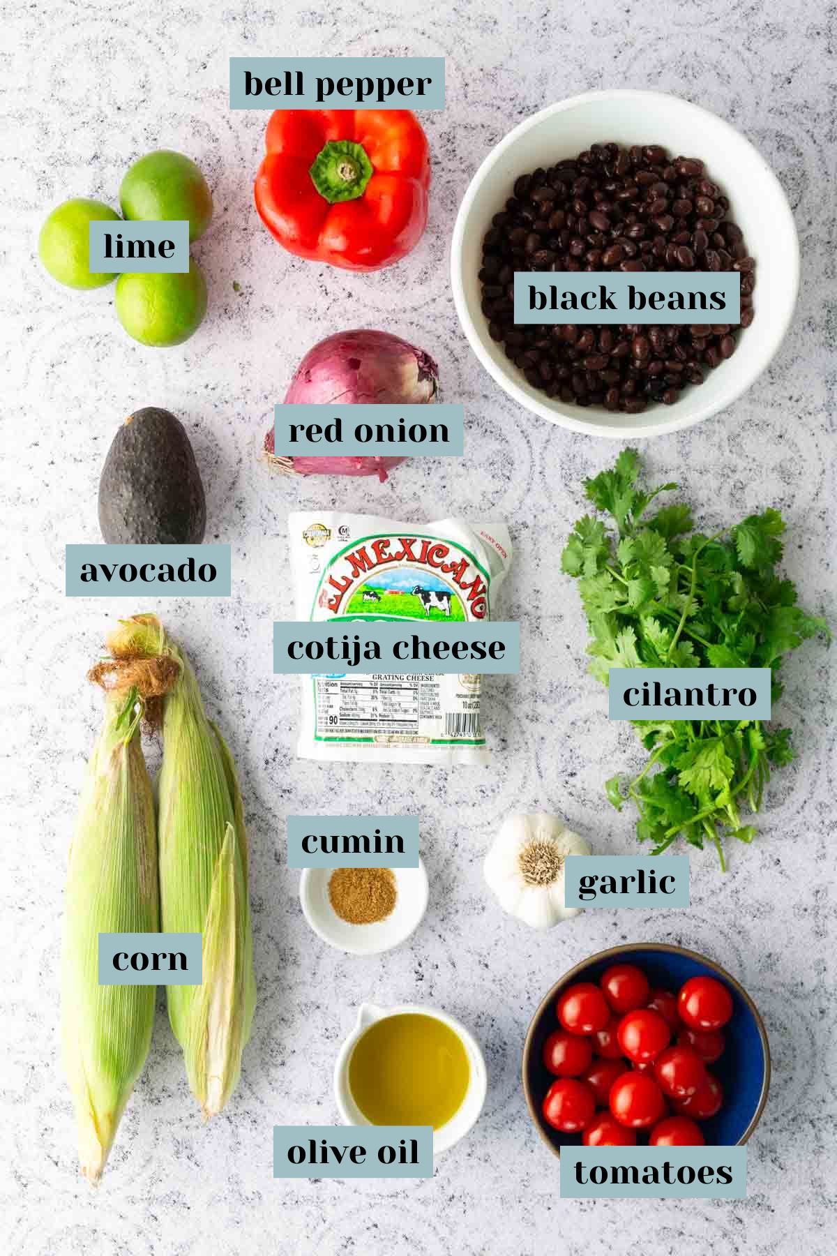 Assorted ingredients for a Mexican-inspired dish, including lime, bell pepper, black beans, red onion, avocado, cotija cheese, cilantro, corn, cumin, garlic, olive oil, and tomatoes.