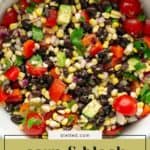 A bowl filled with corn and black bean salad, including diced tomatoes, red bell peppers, avocado, red onion, and cilantro.