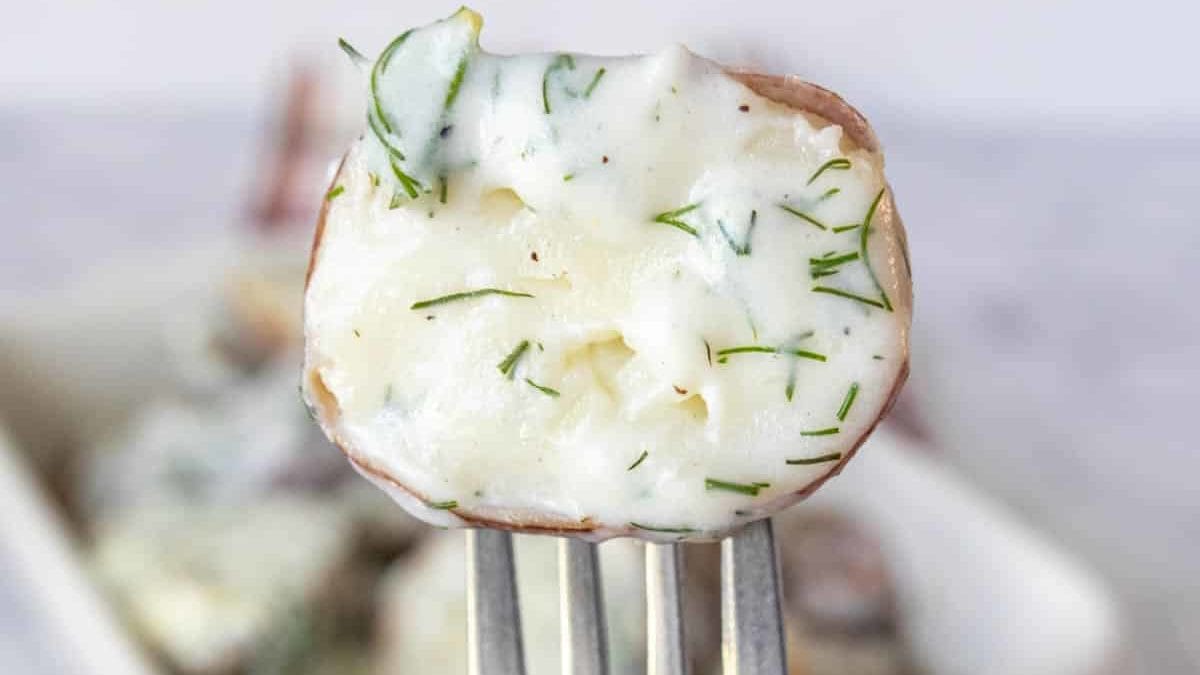 Fork holding up half a small potato with dill cream sauce on it.