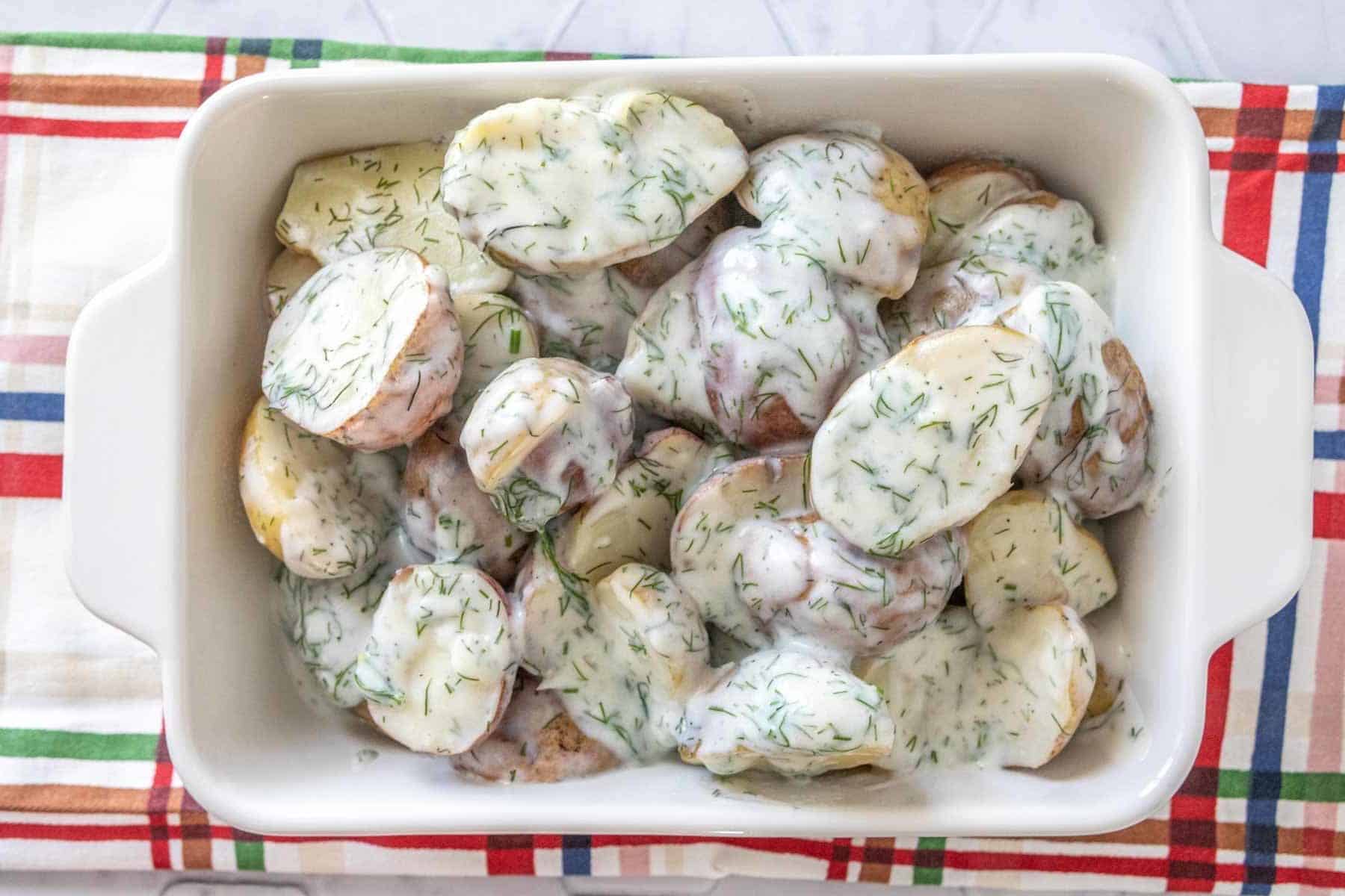 Overhead of dill potatoes in a white dish with a colorful plaid napkin underneath.