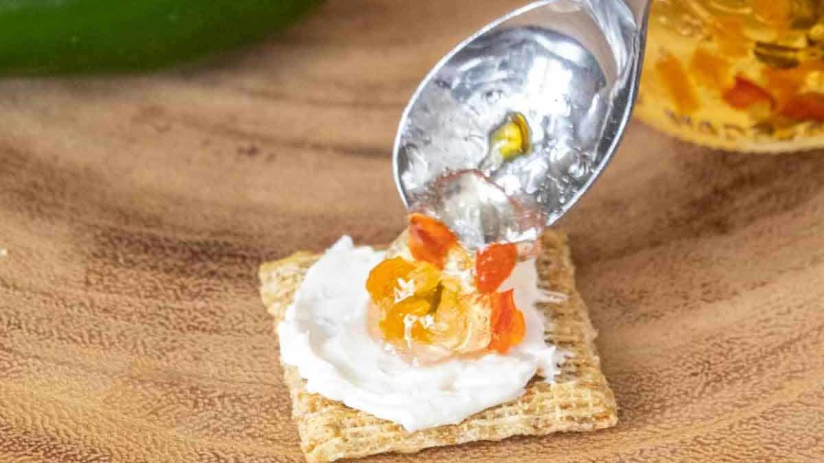 Spooning pepper jelly onto a cracker with cream cheese.
