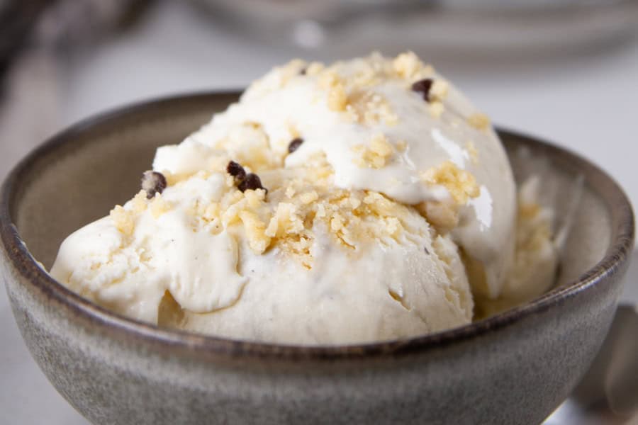 A bowl of vanilla ice cream topped with crumbled cookie pieces, served in a gray ceramic bowl.