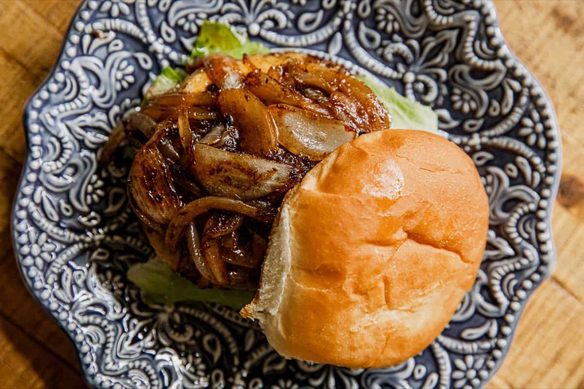 A sandwich with grilled onions and lettuce on a bun is served on a patterned plate.