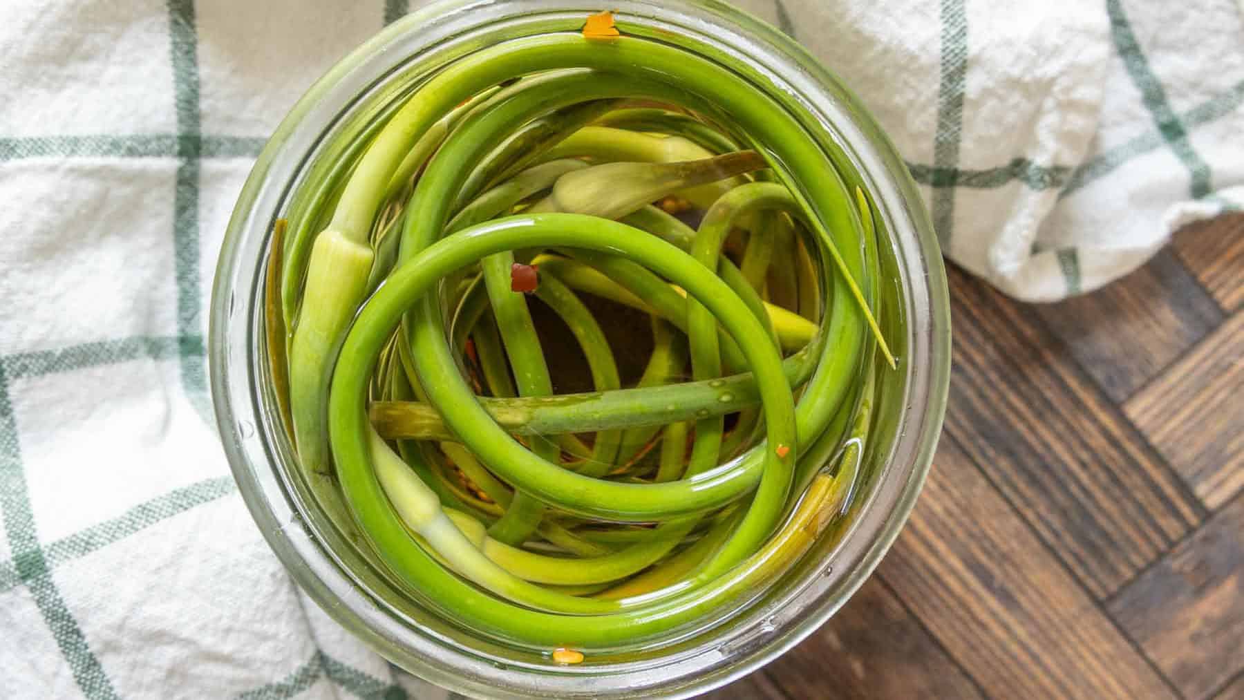 Open jar of pickled garlic scapes from overhead.
