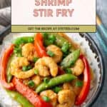 A bowl of shrimp stir fry with red bell peppers and snap peas served over white rice, garnished with chopped green onions.