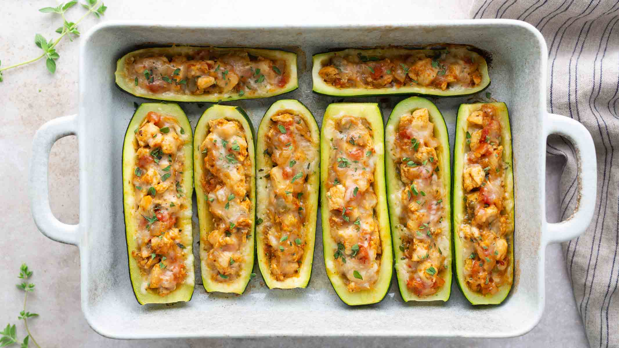 A casserole dish filled with zucchini boats that are stuffed with chicken and cheese.