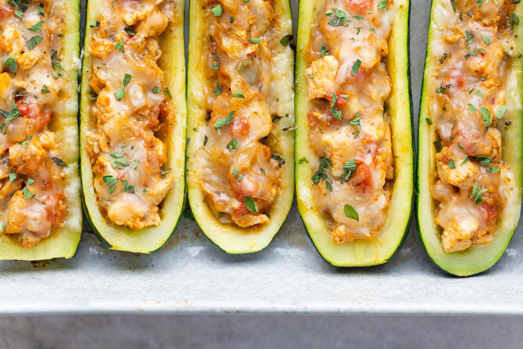 Close-up of zucchini halves filled with a mixture of cheese, vegetables, and herbs, arranged in a baking dish.