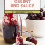 A jar and spoon of cherry BBQ sauce are displayed on a wooden board next to fresh cherries in a white bowl. Text overlay reads, "Cherry BBQ Sauce. Get the recipe at stetted.com.