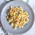 A plate of cavatappi pasta mixed with pieces of chicken, bacon bits, chopped green onions, and a creamy sauce is displayed on a grey plate.