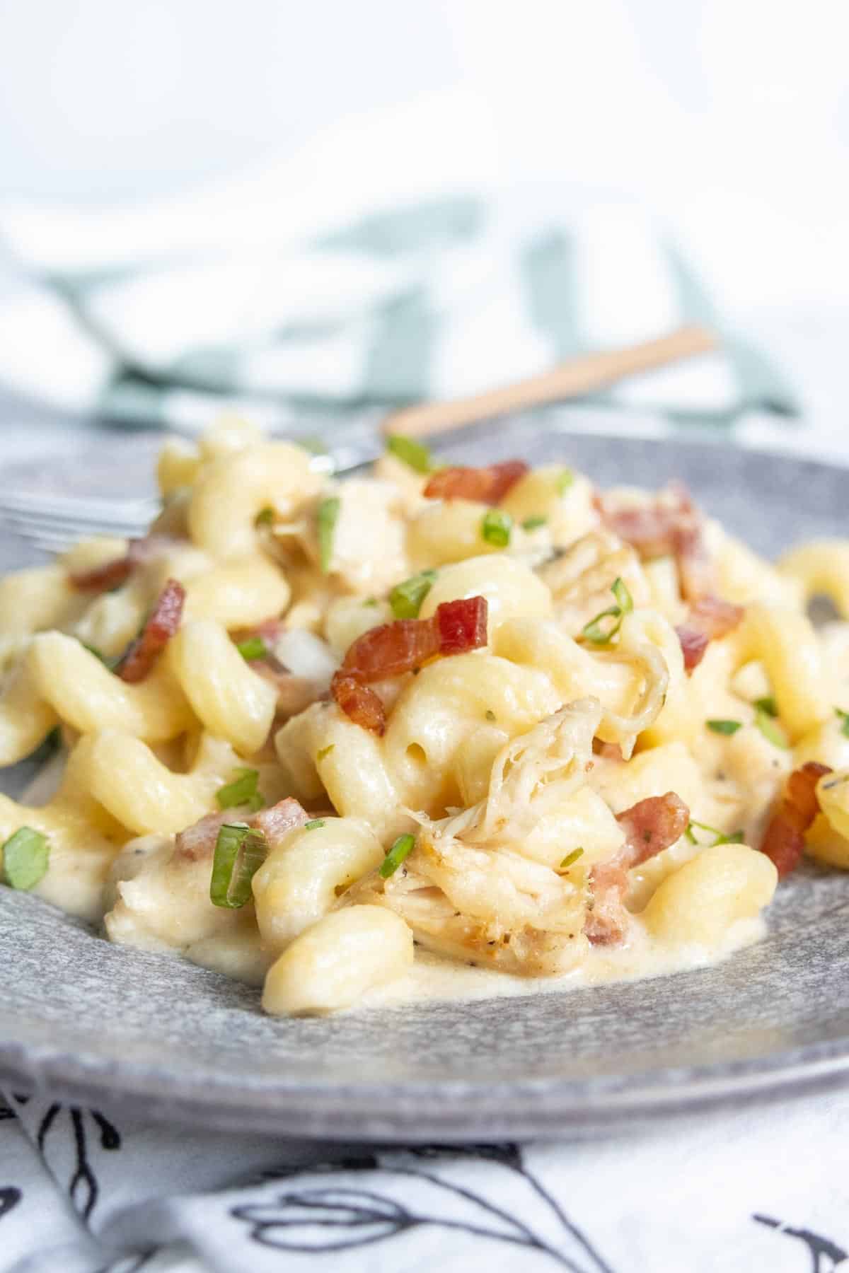 A plate of creamy pasta with pieces of bacon and green herbs, served on a gray dish with a fork in the background.