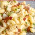 Close-up of creamy chicken bacon ranch pasta garnished with chopped herbs on a gray surface.