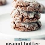 Three peanut butter chocolate crinkle cookies stacked on a white plate, dusted with powdered sugar.