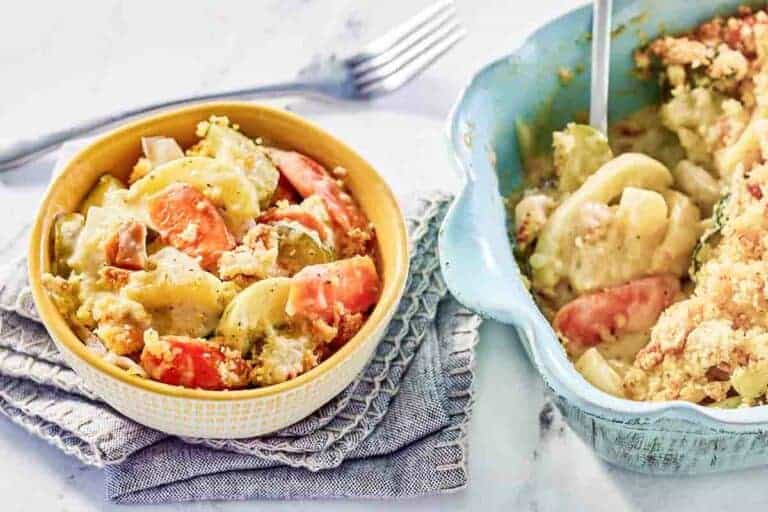 A bowl and baking dish filled with a creamy vegetable casserole containing potatoes, carrots, and a crumb topping, with a fork nearby on a textured napkin.