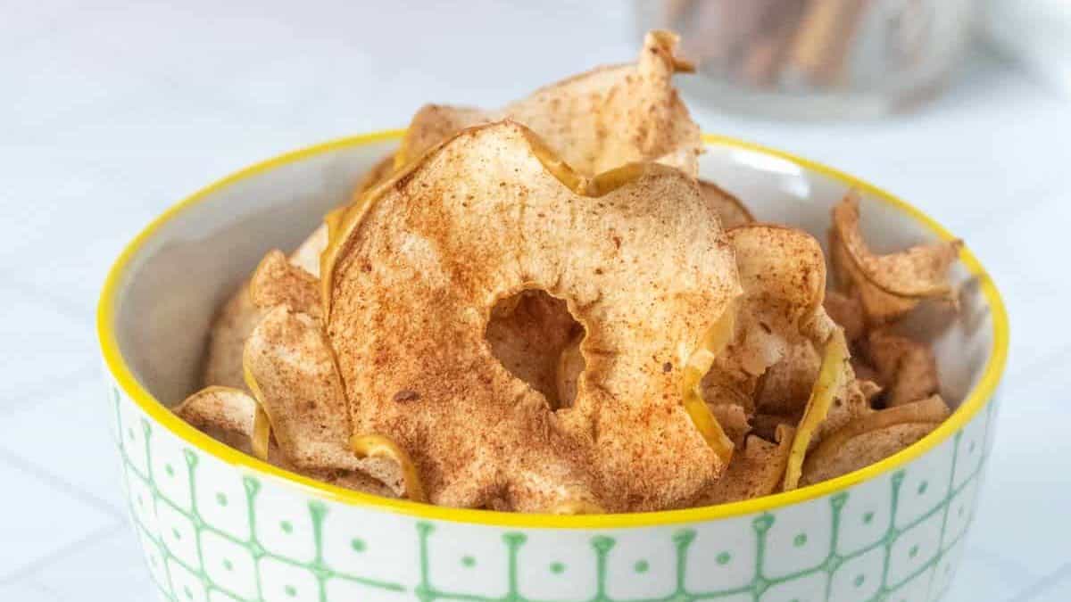 Apple chips in a bowl with cinnamon sticks.