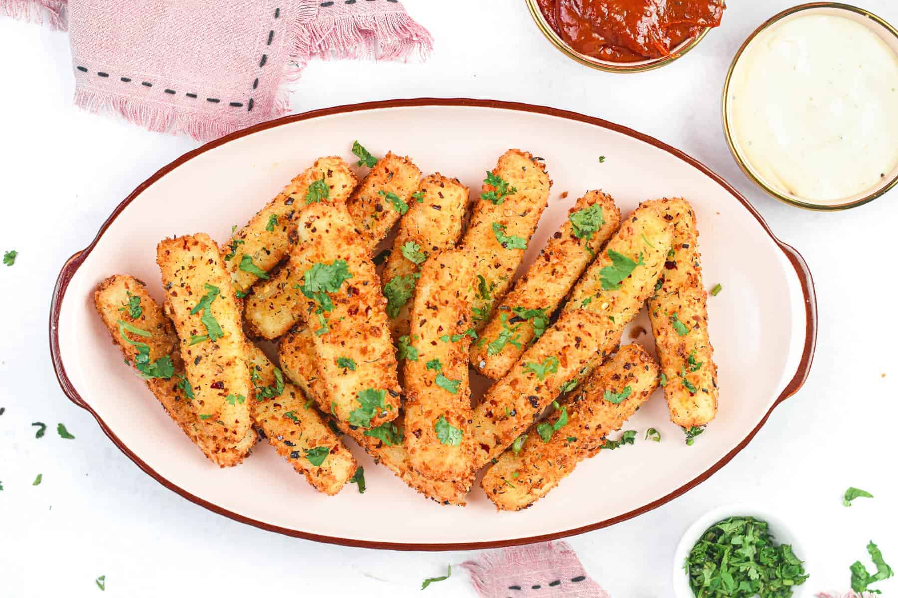 A plate of breaded mozzarella sticks garnished with chopped parsley, served with bowls of marinara and white dipping sauces.