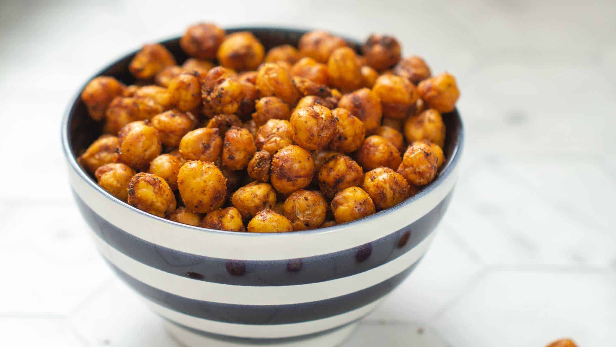A striped bowl filled with roasted chickpeas seasoned with spices, placed on a white surface.
