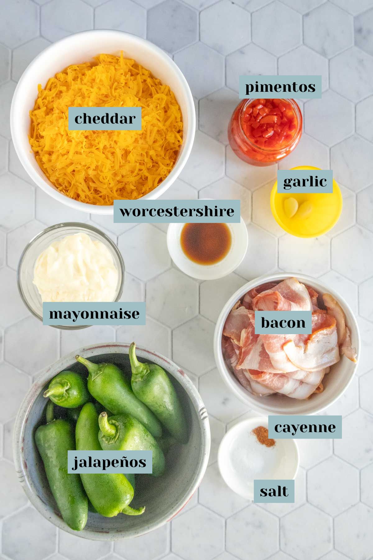 Ingredients arranged on a countertop: shredded cheddar, pimentos, garlic, Worcestershire sauce, mayonnaise, bacon, jalapeños, cayenne pepper, and salt. Labels identify each item.