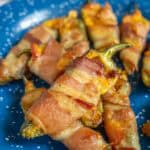 Several bacon-wrapped jalapeño poppers are arranged on a blue speckled plate.