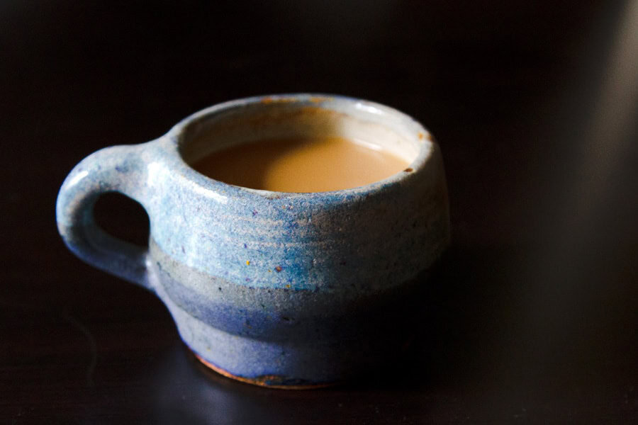 A handmade blue ceramic mug filled with coffee sits on a dark surface.