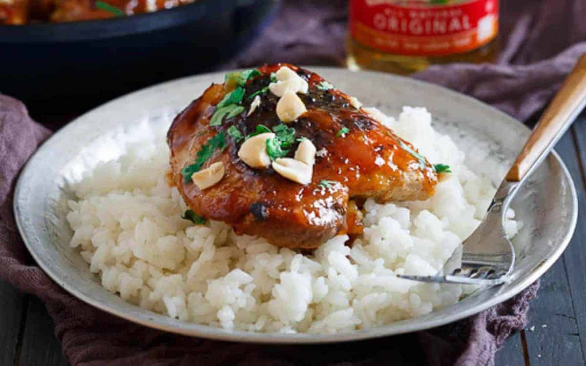 A plate of white rice topped with glazed chicken, chopped peanuts, and herbs, with a fork on the side.