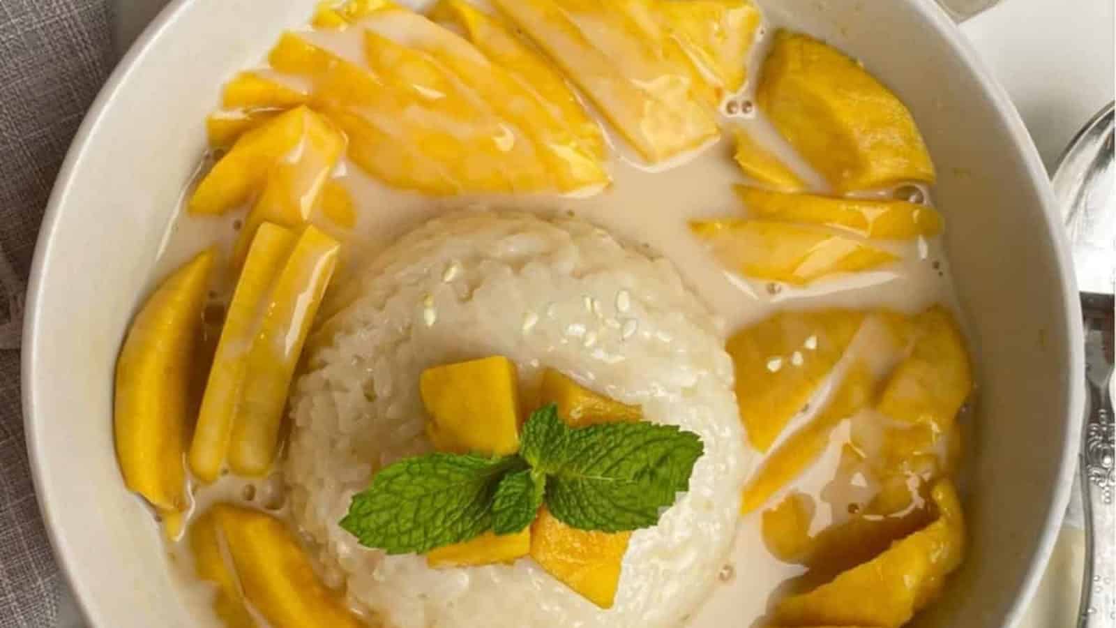 Bowl of mango sticky rice with sliced mango, sticky rice, coconut sauce, and a mint garnish on top.