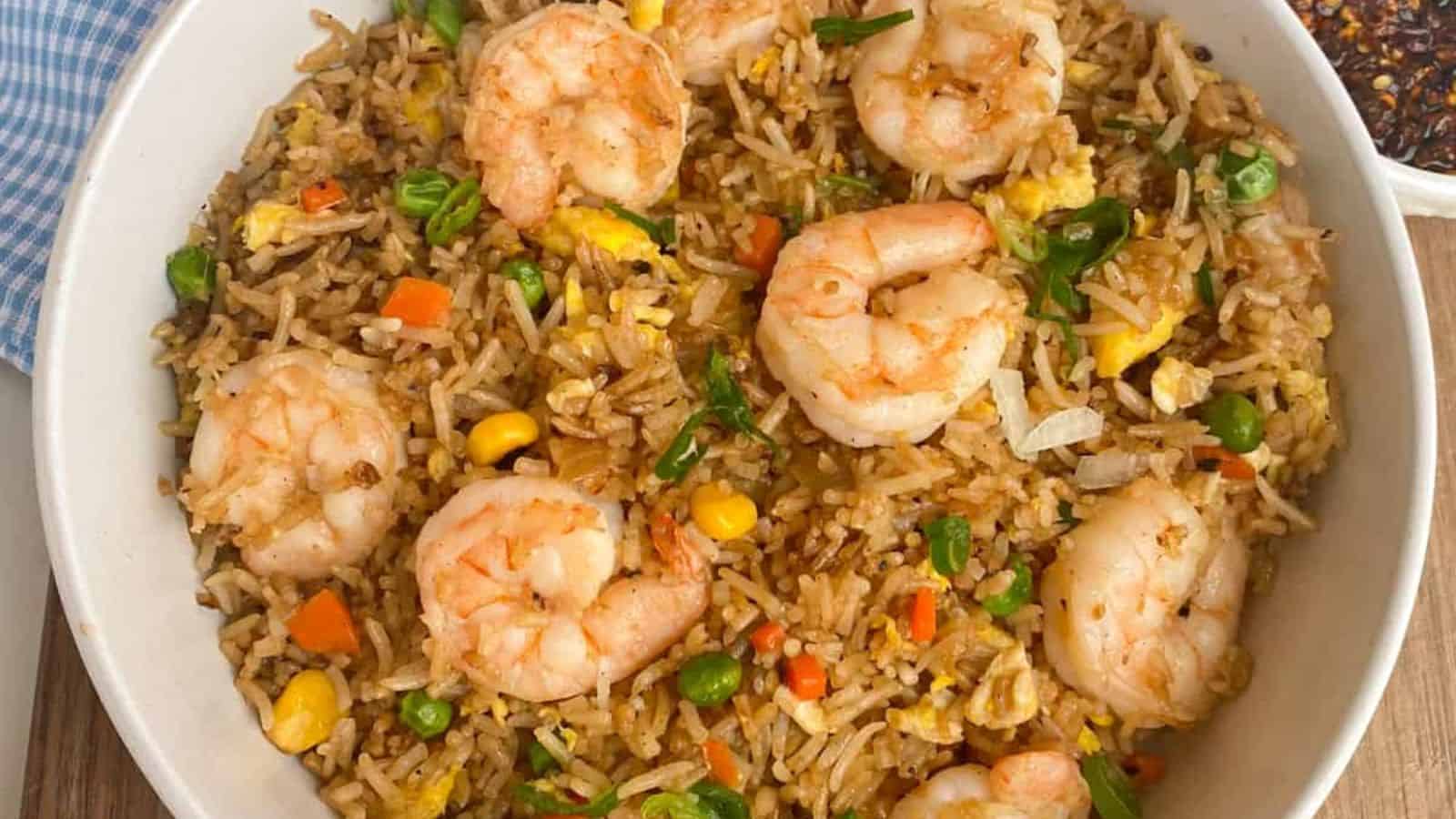 A bowl of shrimp fried rice with peas, carrots, corn, egg, and green onions.