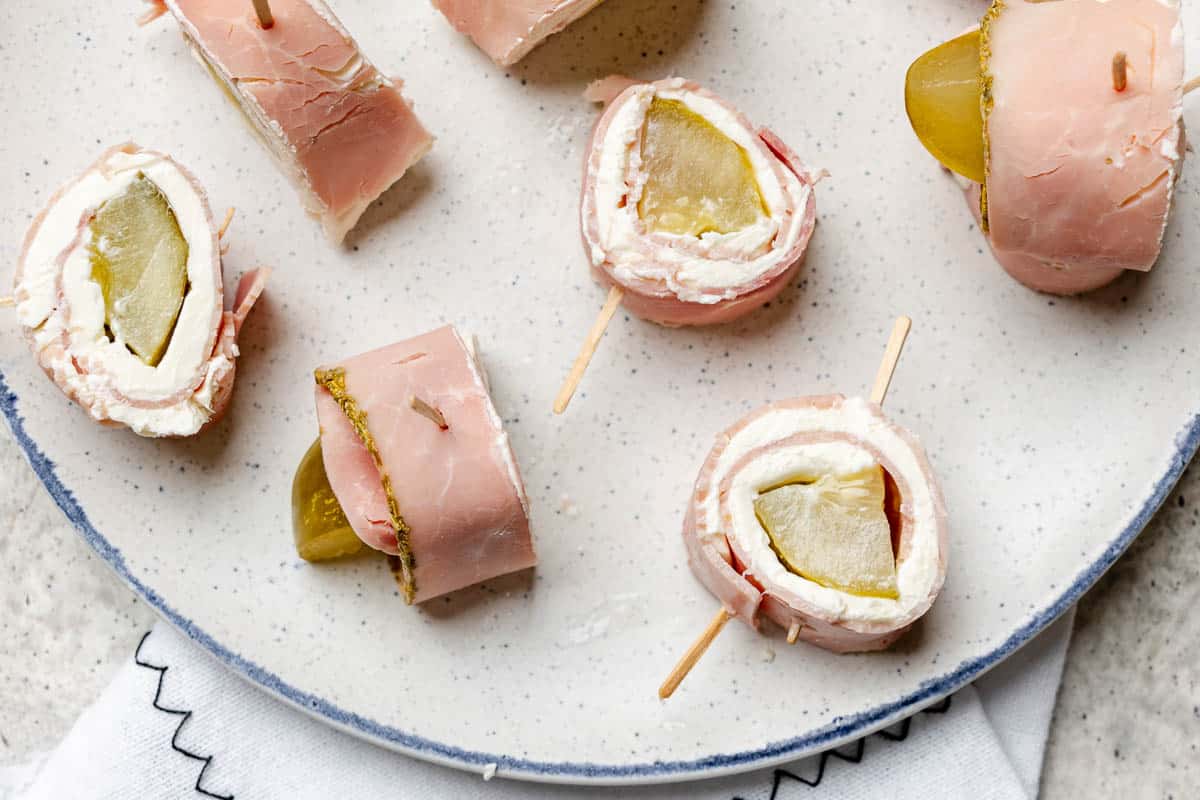 Plate with ham roll-ups filled with cream cheese and pickles, each piece secured with a toothpick.