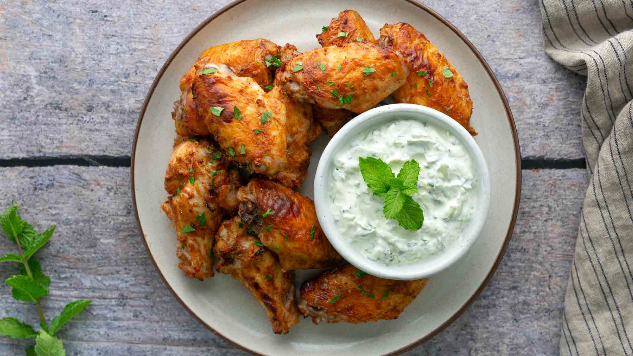 A plate of seasoned chicken wings with cucumber sauce on the side.