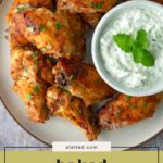 A plate of baked chicken wings garnished with herbs, served with a bowl of creamy dipping sauce topped with mint.