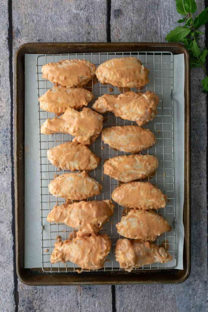 A baking tray with a wire rack holds twelve breaded chicken wings arranged in neat rows on parchment paper.
