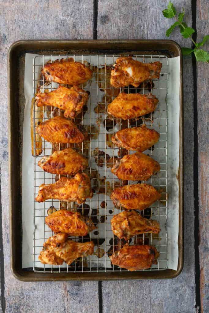 A baking tray lined with parchment and a wire rack holds 16 cooked chicken wings arranged in rows on a wooden surface.
