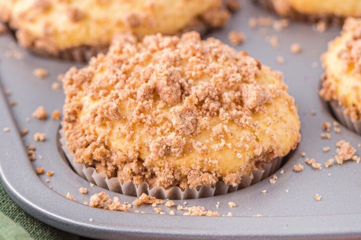 A close-up of a muffin with a crumbly cinnamon streusel topping in a muffin tin.