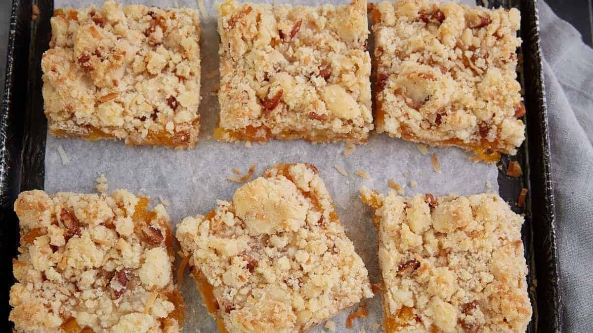 Six rectangular crumb bars with a golden streusel topping are arranged on a parchment-lined baking tray.
