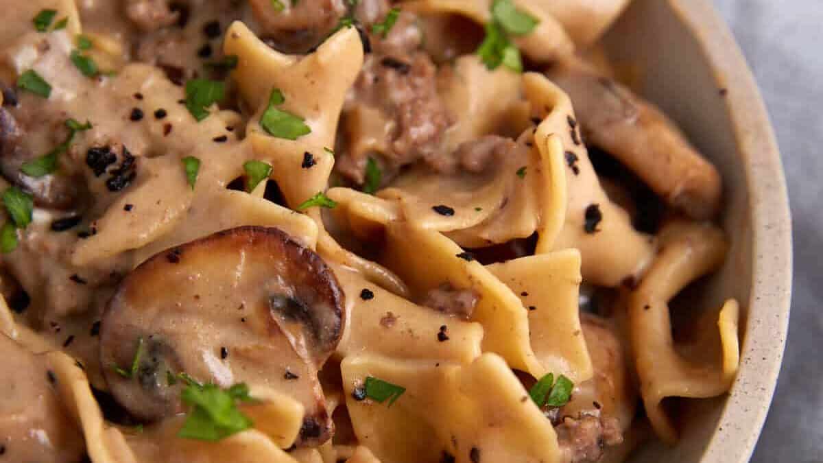 Close-up of creamy beef stroganoff with wide egg noodles, sautéed mushrooms, ground beef, and garnished with chopped parsley.