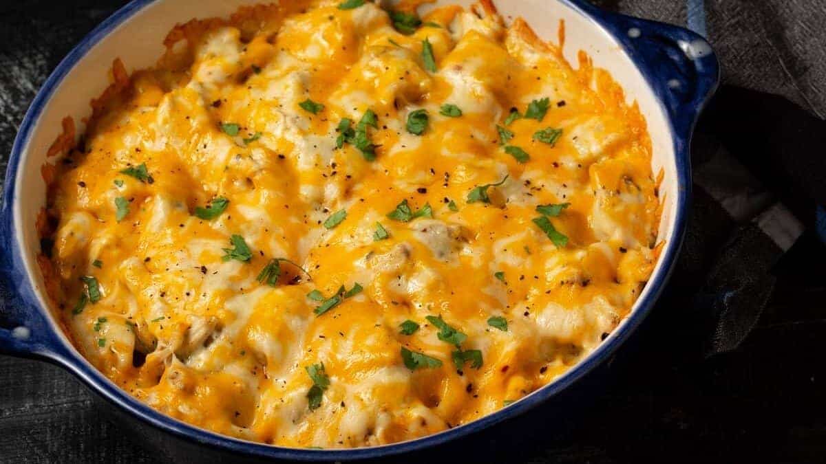 A baked casserole topped with melted cheddar cheese and garnished with chopped parsley in a round blue and white dish.