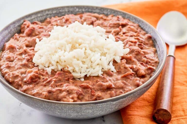 A bowl of creamy red beans with a mound of white rice on top, placed next to an orange napkin and a spoon.