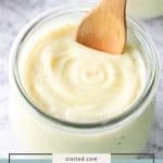 A glass jar filled with creamy homemade chicken soup, with a wooden spoon resting inside, on a light surface.