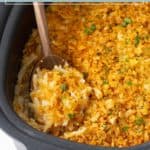 A wooden spoon serves cheesy potatoes topped with crushed chips in a black crockpot. Text above reads “crockpot cheesy potatoes.”.