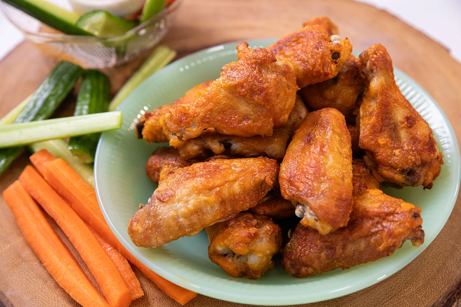 A green plate of fried chicken wings is served with celery and carrot sticks on a wooden surface.