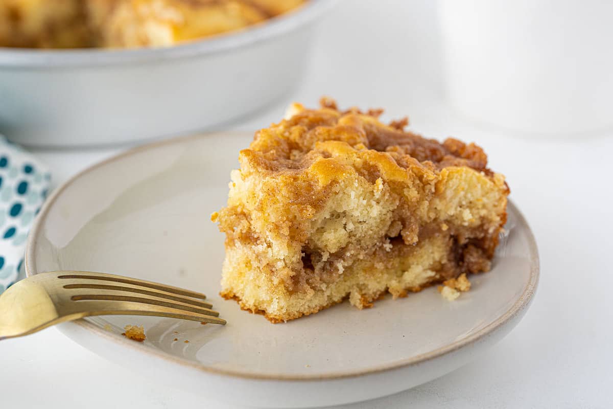 A slice of coffee cake with cinnamon filling on a white plate, next to a gold fork.