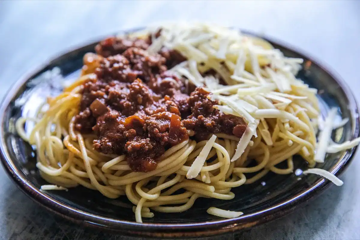 A plate of spaghetti topped with meat sauce on one side and shredded cheese on the other.