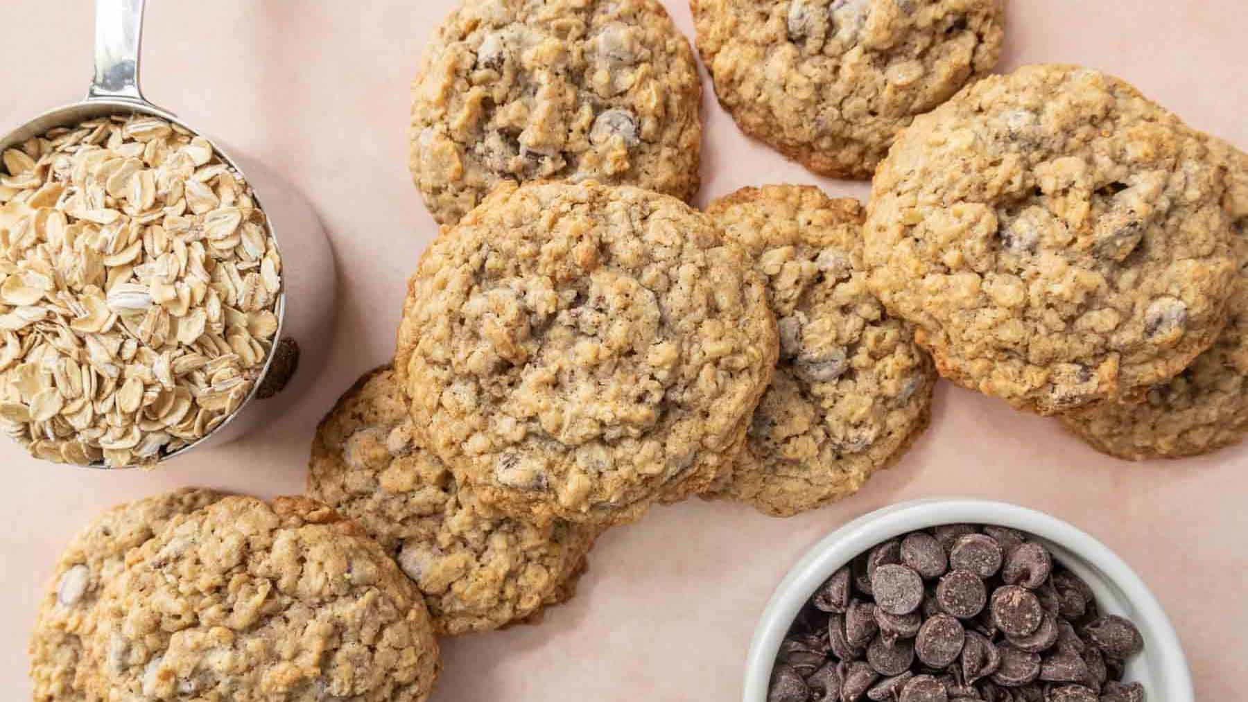 Oatmeal chocolate chip cookies are arranged on a surface, with bowls of chocolate chips and oats nearby.
