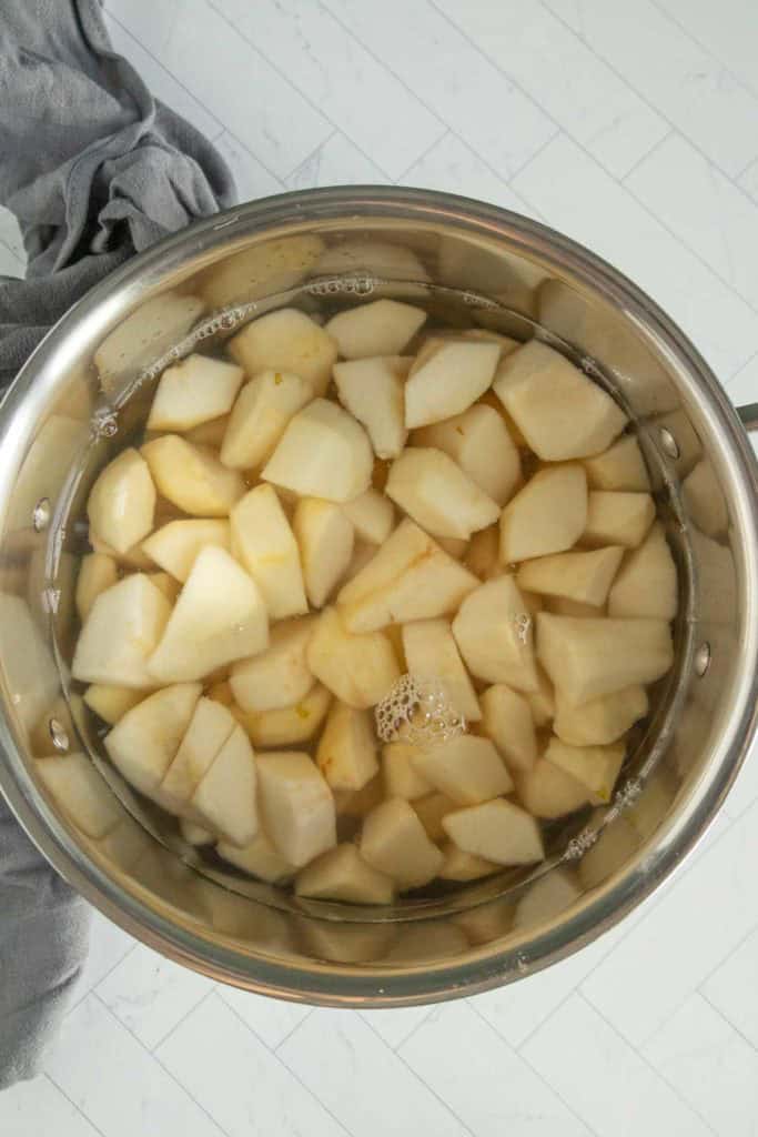 A stainless steel pot filled with peeled and chopped pears soaking in water, placed on a light-colored countertop.